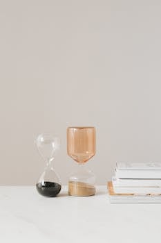 白色的桌子上，美丽的现代沙漏里装着黑色和玫瑰色的沙子，旁边放着一堆书