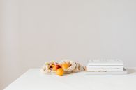 Jute sack with natural ripe apricots on white table composed with stack of various books and magazines
