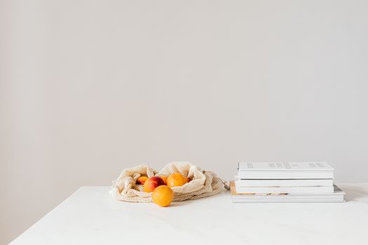 Jute sack with natural ripe apricots on white table composed with stack of various books and magazines