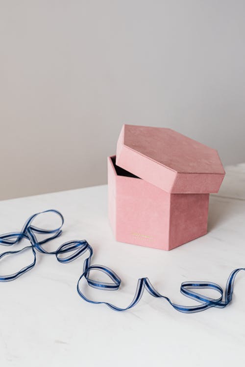 From above of original pink hexagon shaped gift box placed on marble table with blue organza ribbon