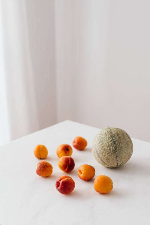 From above composition of whole melon and ripe colorful apricots placed on white table