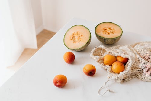 Jute sack with ripe apricots on table near halved appetizing melon