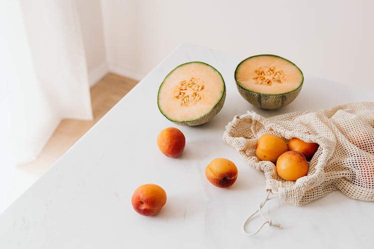 Jute Sack With Ripe Apricots On Table Near Halved Appetizing Melon