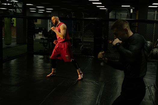 Two men practice boxing techniques in a dimly-lit gym, focusing on form and agility.
