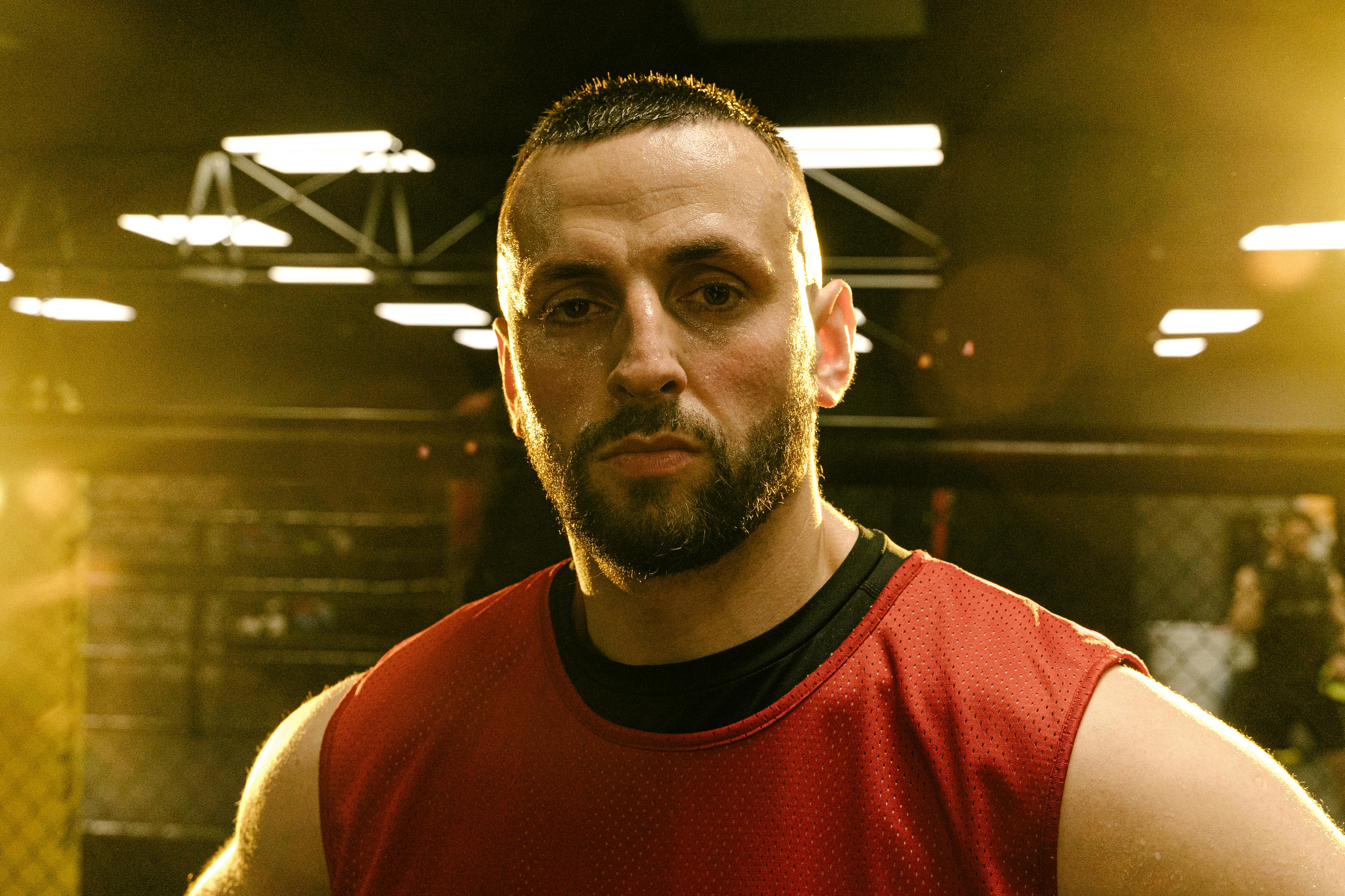 A focused and serious man in a gym setting, illuminated by warm lighting.