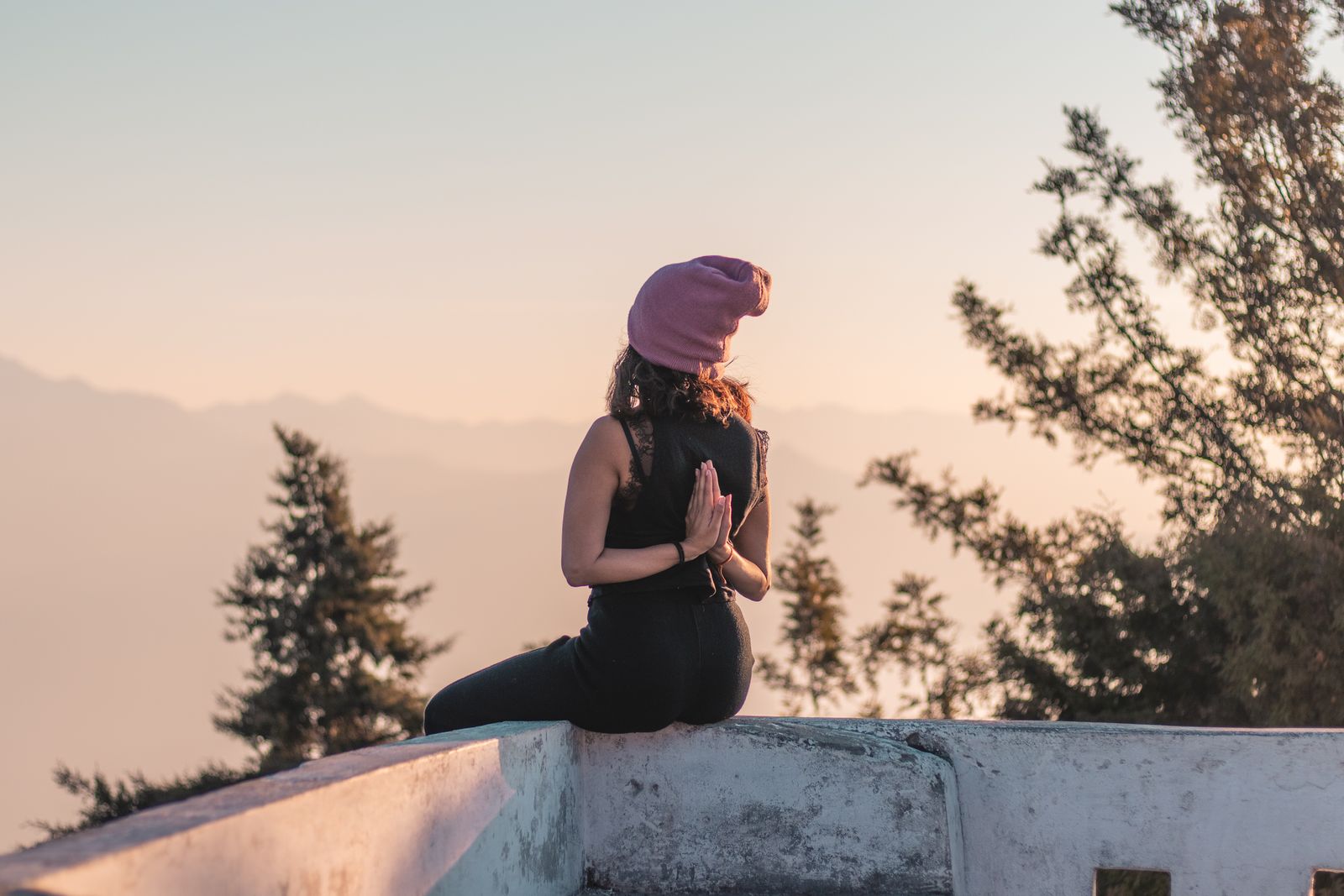 Person meditating in a seated prayer pose on a rooftop in Rishikesh, reflecting the contemplative practice behind karma yoga