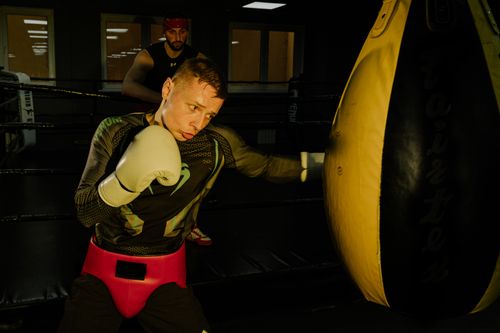 Free A determined boxer practicing punches on a heavy bag with a trainer in the gym. Stock Photo