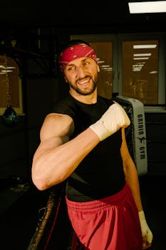 一位开朗的拳击手面带微笑地站在拳击台上，双手缠着绷带，显得自信而满足