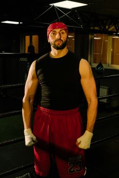 A focused boxer standing confidently in the ring wearing a black tank top and red shorts.