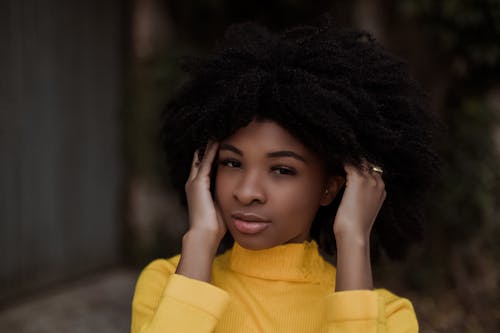 Young dreamy African American black haired female touching curly hair while standing on street