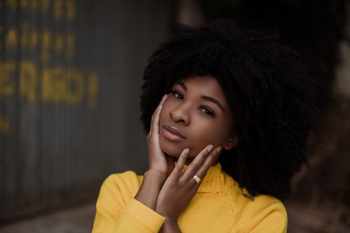 Free Young African American female looking at camera and thinking while standing on street near wall Stock Photo
