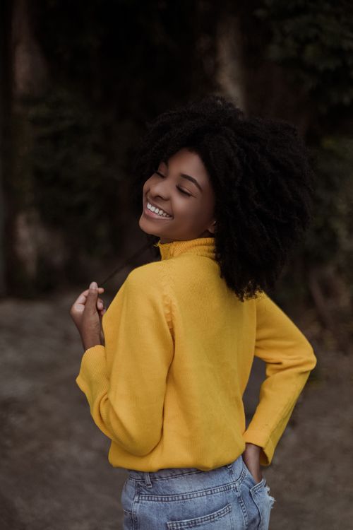 Free Back view of black female with curly hair wearing yellow sweater and jeans standing with hand in pocket Stock Photo