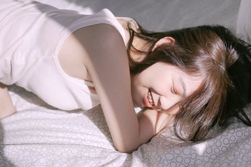 Woman in White Tank Top Lying on Bed