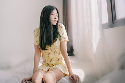 Woman in Yellow Dress Sitting on Bed