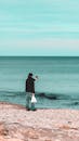 Back view of full body unrecognizable man with smartphone in hand taking photo of sea