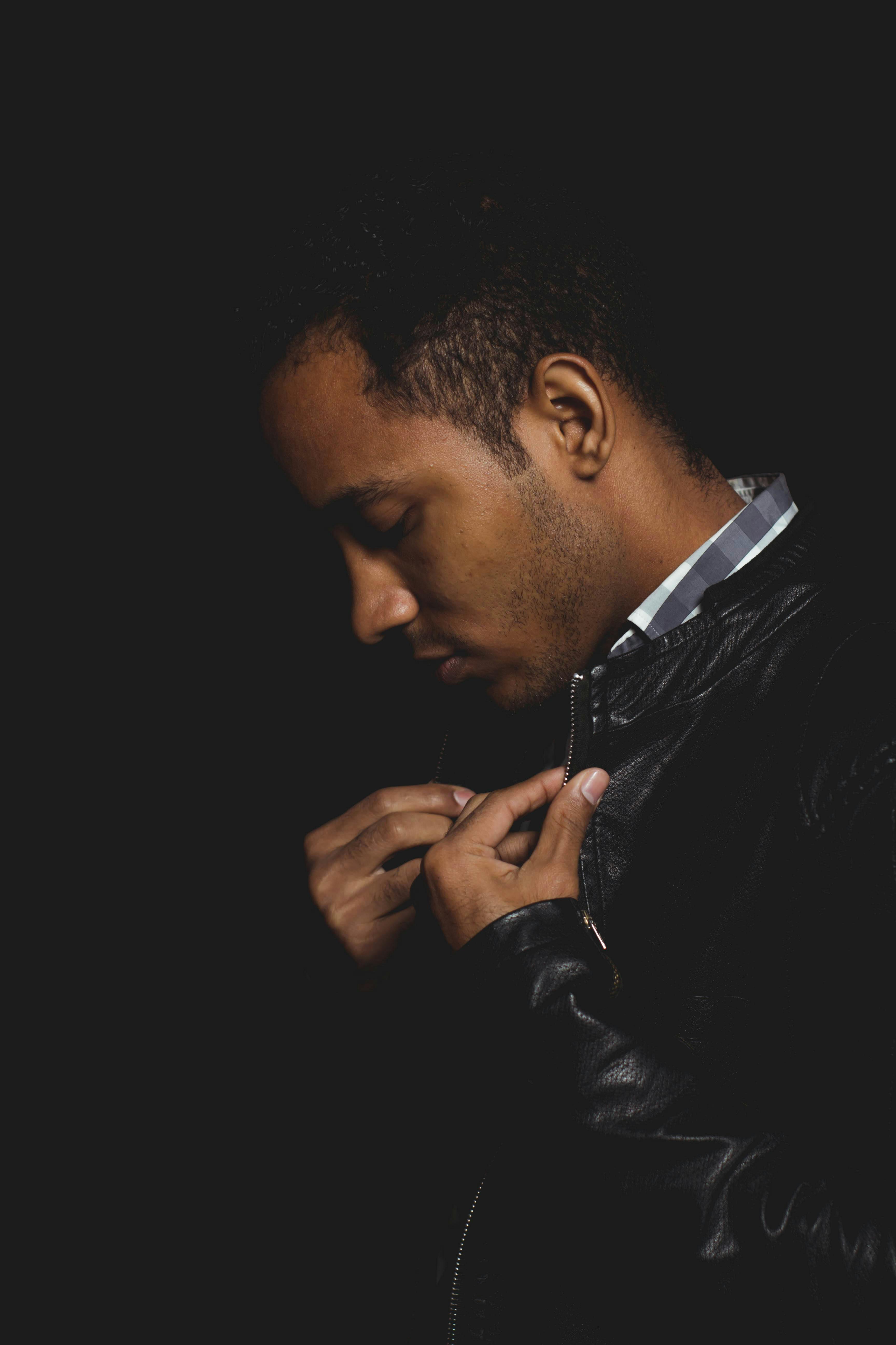 Close-up portrait of a man in a leather jacket, adjusting collar, against dark background.