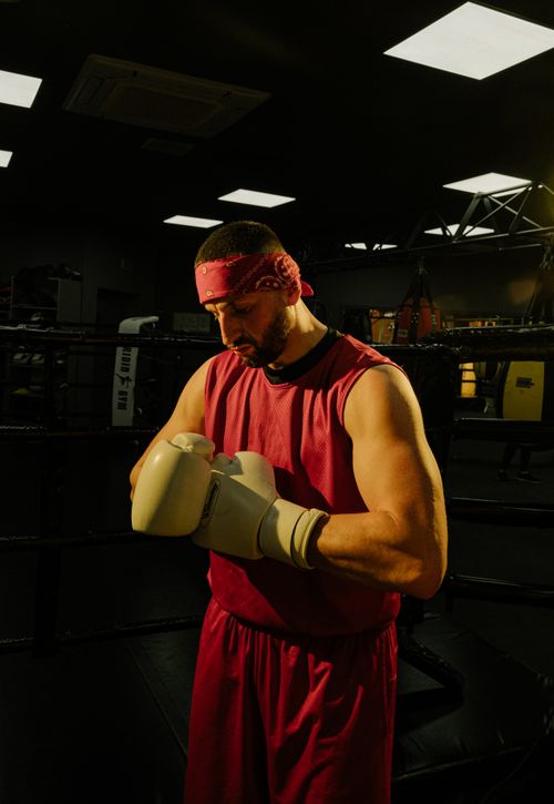 Free Focused boxer adjusts gloves in a dimly lit gym, preparing for a training session. Stock Photo