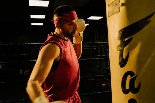 A muscular man with a beard and bandana practices boxing with a punching bag in a gym.