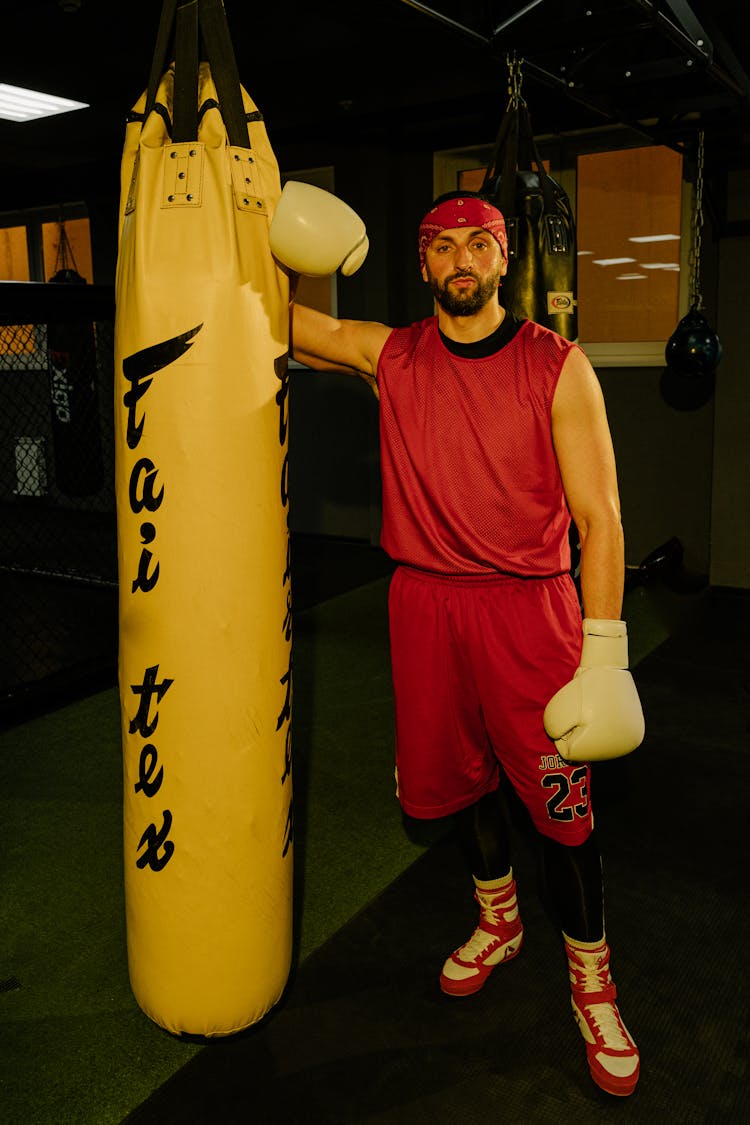 Man In Red Tank Top Standing Beside A Punching Bag