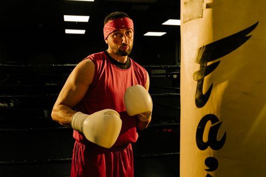 Male boxer in red attire practicing in a gym with a punching bag.