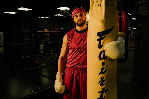 Free Boxer in red gear training with a punching bag in a dimly lit gym, ready for a fight. Stock Photo