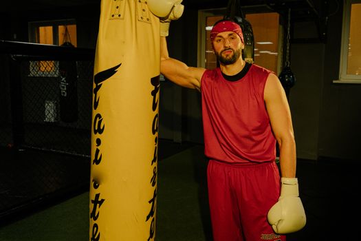 Athlete in red sportswear posing indoors with a punching bag, showcasing fitness and strength.