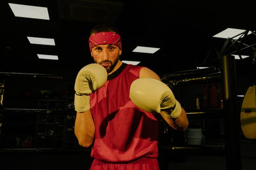 Free Boxer wearing a red bandana and gloves practicing in a dimly lit gym. Stock Photo