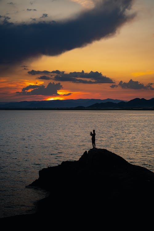 Silhouette of a Person Standing on the Rocky Shore