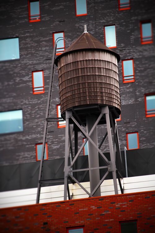 Free A classic rooftop water tower set against a modern building facade with vibrant red window frames. Stock Photo
