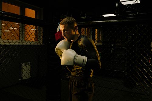 Free Focused boxer practicing in a dim-lit gym cage, showcasing determination and skill. Stock Photo