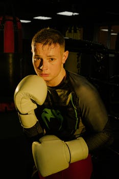 Confident young boxer poses in gym wearing gloves. Perfect for sports and fitness themes.