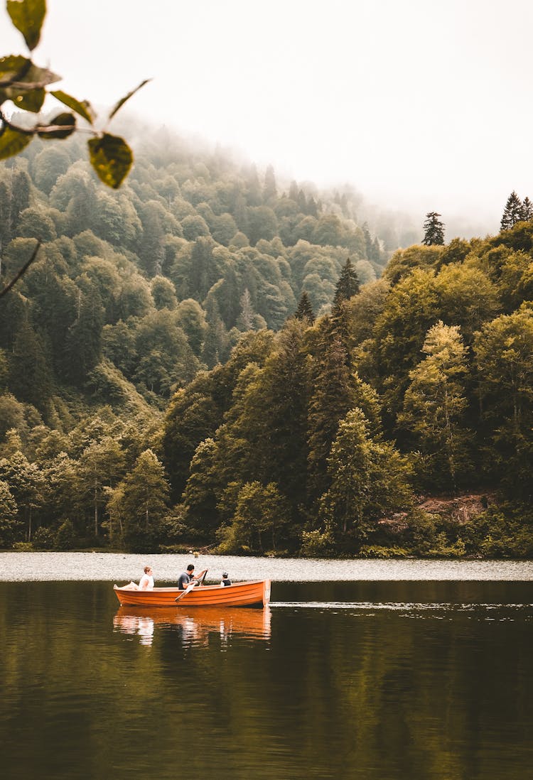 People Floating On Small Boat Along Calm River In Nature