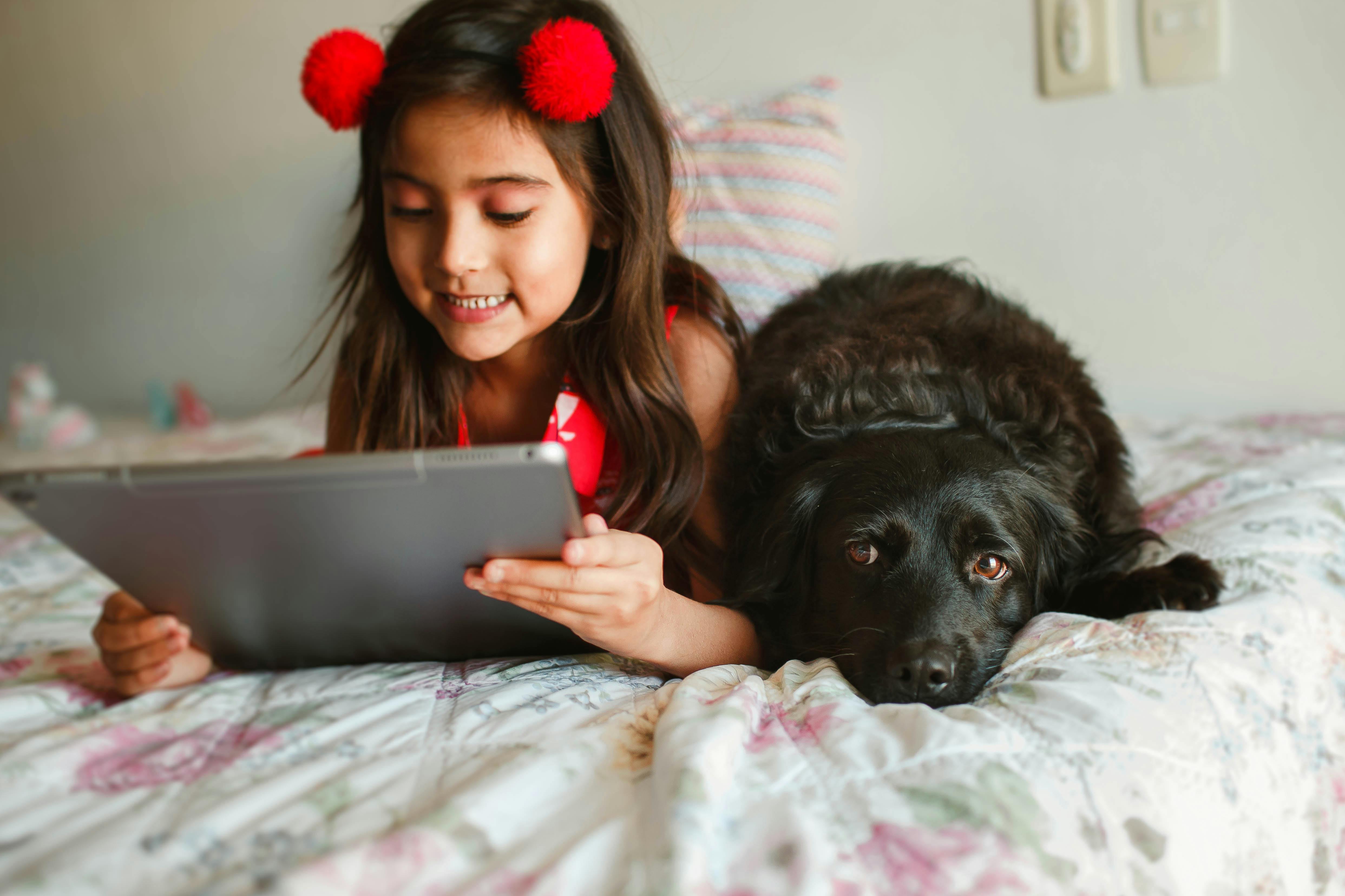 crop smiling girl with tablet resting on bed with spaniel