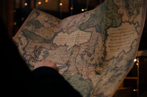 From behind anonymous person examining antique world map printed on large paper in blue colors in dark room