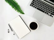 Laptop near cup of coffee and blank notebook in office