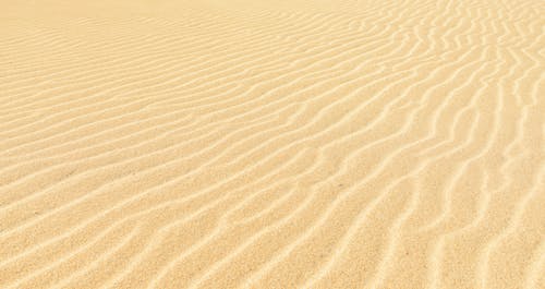 From above textured background of sandy terrain with uneven rippled surface in summertime in afternoon