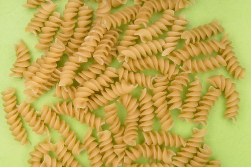 Free Uncooked rotini pasta spirals scattered on a bright green surface, ideal for culinary themes. Stock Photo