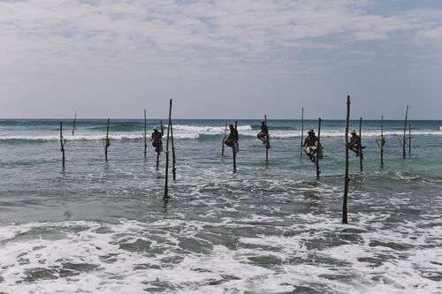 Free Stilt fishermen perched over ocean waves in Sri Lanka, showcasing a timeless cultural tradition. Stock Photo