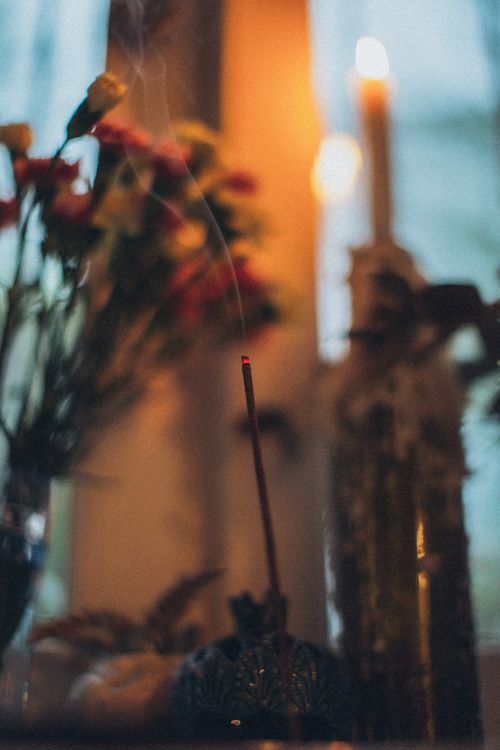 Free Burning sandalwood stick with aromatic smoke near vase with blossoming flowers and glowing candle at home Stock Photo
