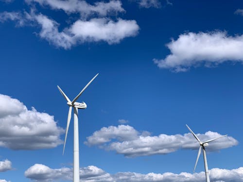 Free Low angle of white modern windmill turbines generating energy against cloudy blue sky on sunny day Stock Photo