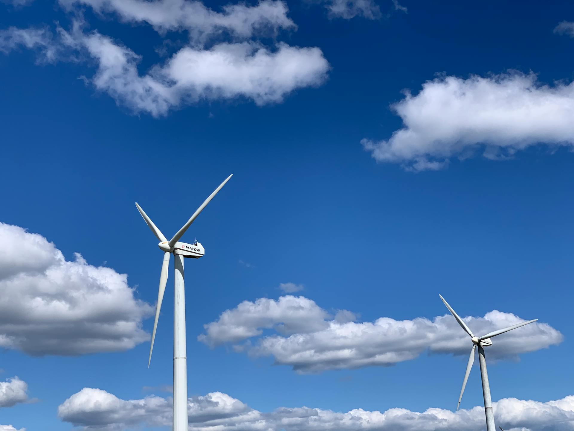 Low angle of white modern windmill turbines generating energy against cloudy blue sky on sunny day