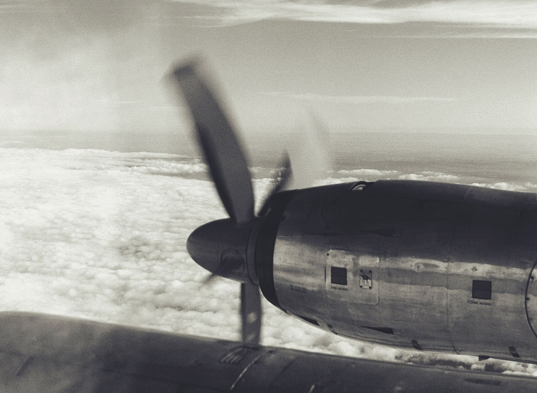 Black and white photo of a vintage aircraft propeller in motion above the clouds, showcasing classic aviation.