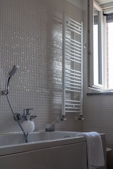 Bright bathroom with a tub, towel rack, and open window, showcasing a contemporary interior style.