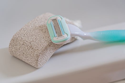 Detailed image of a razor and pumice stone placed on the edge of a bathtub, emphasizing self-care tools.
