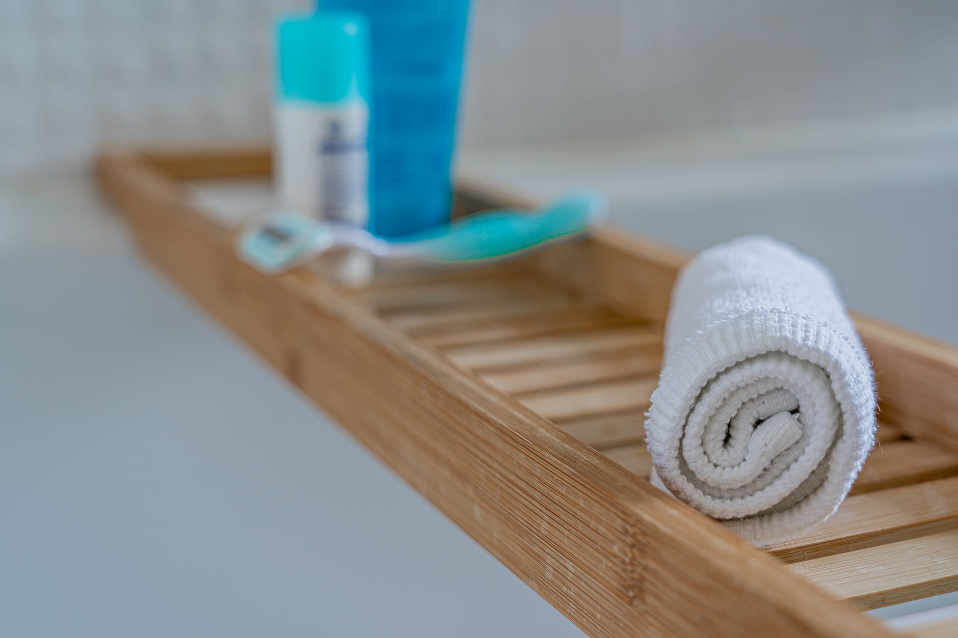 Rolled towel and bath essentials on a wooden tray with a minimalist aesthetic.