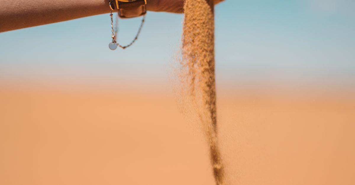 Rüyada Zamansızlık Görmek - Rüya Tabiri ve Anlamı - A watch on a hand pouring sand in the Moroccan desert under a clear blue sky.