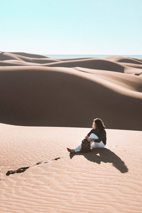 Woman in White Long Sleeve Shirt Sitting on Brown Sand