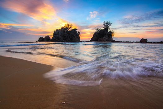 Spectacular view of bright cloudy sky above rippled sea with rocks and sandy shore at sunset