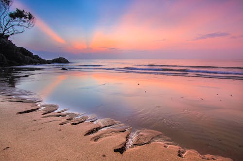 Scenery view of rippled ocean near holes on sandy shore under colorful cloudy sky at sundown