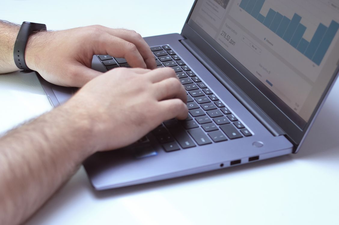 Free From above side view of crop unrecognizable male marketer working on netbook while using analytical software in office Stock Photo